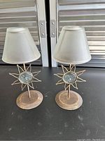Pair of sun motif table lamps with frosted conical shades on a metallic base with textured circular center.