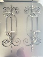 Photo of two black metal wall candle holders featuring scrollwork and circular candle plate support.