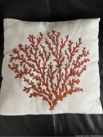 Close-up image of one white square decorative pillow with orange coral embroidery.