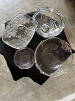 Four clear glass dishes with floral patterns displayed on black fabric