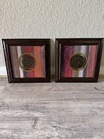 Pair of brown square picture frames with colorful stripe and leaf artwork and a central circular metal ornament.