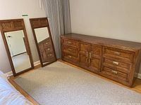 Wide shot showing the dresser and two matching mirrors standing beside it against a wall on hardwood floor with curtain and door in the background.