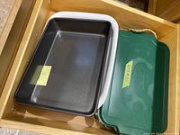 Stack of 3 clear glass Anchor Hocking baking dishes seen partially inside a wooden drawer with a dark non-stick metal baking pan beside them.