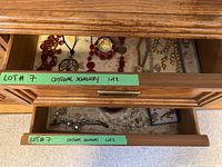 Photo of top wooden drawer with assorted necklaces including red beaded, silver pendant on black cord, and others; some bracelets visible; floral drawer lining.