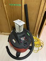 Craftsman wet/dry vacuum with hose and yellow extension cord, pleated filter on top of vacuum, showing 5.5 HP label on unit.