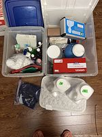 Photo showing two clear plastic storage bins containing assorted self-care items such as bottles, cotton balls, medicine box, hot water bottle, and white containers
