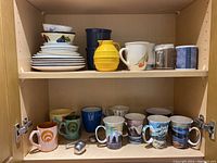 Shelf with two rows of assorted ceramic mugs and small plates.