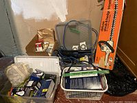 Photo showing assortment of boxed light bulbs, timers, blue extension cords, weather stripping supplies in rolls, and boxed deluxe hedge trimmer in orange packaging.