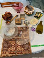 Lot items spread on table: pink glass bowl, clear bowls, vintage-style runner, dishes, basket, small boxes