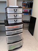Multiple stacked plastic storage drawers with transparent fronts and black handles, placed against a wall in an office setting