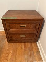 Front view of one bedside table showing two drawers with brass inset handles and wood grain finish.