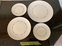 Four plates of different sizes showing grey scroll pattern and silver edging on white bone china surface.