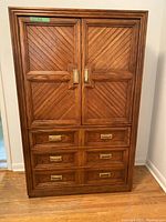 Front view of closed two-door wardrobe with three exterior drawers and brass-tone recessed handles