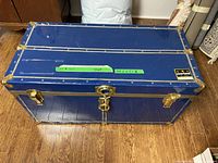 Closed view of blue vintage trunk with gold-tone corners and locks, brand label visible.