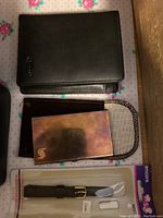 Photo of two leather wallets, a metal business card holder with pouch and a black leather replacement watch band.