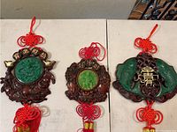 Three Asian-style wall decorations with red hanging tassels shown on a white surface