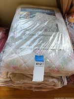 Photo showing the DreamStyles quilted bedspread in original packaging with floral pattern and label visible.