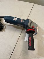 Side view showing Bosch branding and handle with power cord, angle grinder with attached disc.