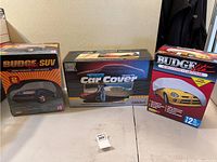 Three boxed semi-custom car covers displayed on a table for various vehicle types including SUV and small car.
