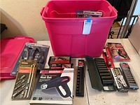 Overview of the lot including pink plastic storage bin with tools and accessories on and around it
