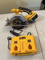 Photo showing DeWalt cordless circular saw with battery attached and DeWalt yellow charger beneath it on a table.