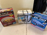 Three original boxed car covers from Duro and Budge brands, placed on table in front of beige wall.