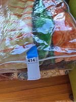Photo of multicolored floral patterned blanket and bedding set inside clear plastic packaging showing warm shades of orange, green and beige.