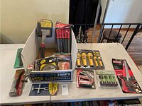 Full view of multiple tools including flashlights, tarps, wrenches, cutting tools, and edge guides displayed on a table.