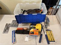 Overview of lot showing large plastic storage container with toolbelt inside, multiple small tool kits, flashlight, and boxed batteries arranged on a table.