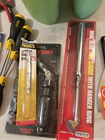 Photo showing yellow and black screwdrivers, pneumatic scraper, and dual head tire gauge packaged with hanger ring.