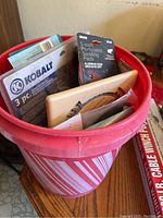 Red bucket filled with various packaged sanding pads, saw blades, and tool accessories.