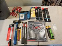 Full overview of lot contents spread on flat surface including hammer, saw blades, wrench set, pliers, utility knife, rip fence guides