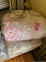 Two queen size comforters stacked, one with colorful abstract pattern and another with beige floral design, both in plastic packaging.