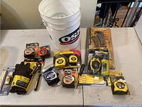 Lot of various measuring tapes, gloves, pencils, wrenches, and tools on table.