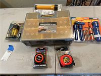 Plastic storage case with compartments, three tape measures, and multiple flashlights still in original packaging.