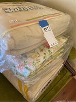 Three folded blankets stacked including a beige Caprice blanket in plastic wrapping, a floral patterned blanket, and a cream or beige blanket.
