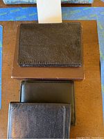 Three men's wallets: one dark brown textured wallet on top of a brown box, two black leather wallets placed side by side below the box.