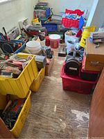 Overview of room with multiple plastic bins, buckets, totes and toolboxes filled with various items