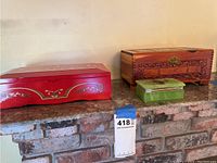 Three trinket boxes displayed on brick surface: red box with floral design, medium carved wood box, small green box.