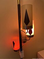 Close-up showing the three cylindrical glass shades in red, white, and orange, each with black diamond motifs, lit and attached to the pole lamp