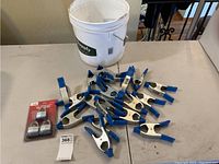 Photo showing collection of spring clamps with blue padded handles arranged on table with white bucket