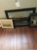 Photo showing all three framed pictures on floor, largest being a dark framed embossed art, plus a colorful mosaic and a beach photo.