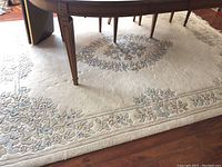 Full view of ivory wool area rug under table showing floral pattern and some staining.