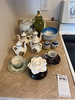 Photo showing decorative bottles, green glass jar, blue and white bowls, salt and pepper shakers, porcelain teacup and saucer, white ceramic flower ornament, and large white vase.