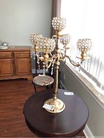Front view of the 30-inch brass four-armed candelabra resting on a wooden round table, showing crystal beaded globes and hanging crystal pendants.