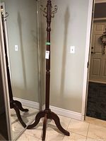Full view of wooden hall tree showing tripod base and height, placed near a wall and mirror.