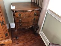 Full view of the three drawer wooden end table showing bowed drawer fronts, brass handles, and floral edge detail.