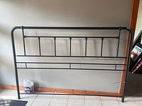 Full frontal view of the black metal king size headboard showing design and size in relation to tiled floor and walls.