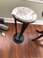 Full view of plant stand showing oval marble top and three-legged black metal frame with lion head decorations near top of legs.