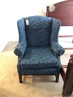 Front view of a blue upholstered wing chair with floral pattern showing overall shape and condition.